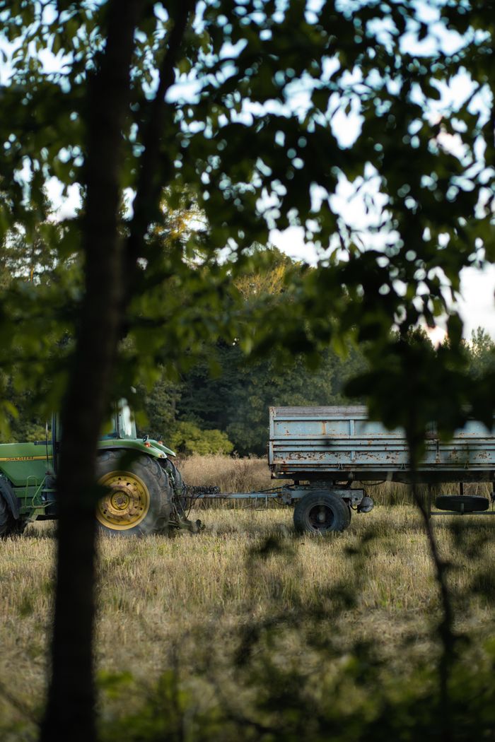 A tractor with a trailer in a rural countryside setting, surrounded by trees in Central Bohemian Region, Czechia.