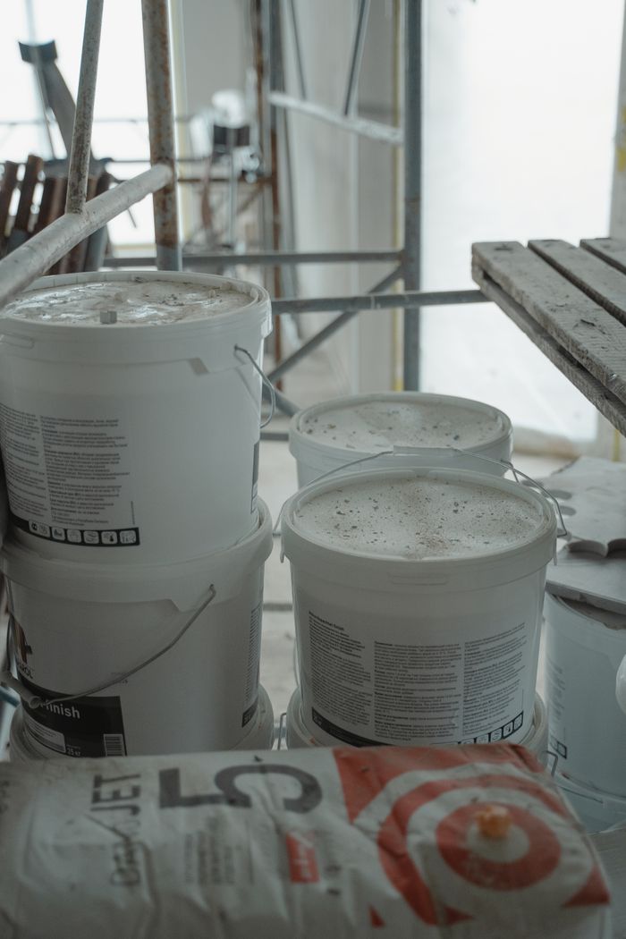 about-us-01 Several white paint buckets stacked in an indoor construction area with scaffolding.