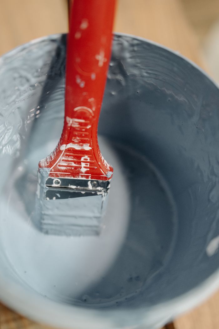 about-us-02 A red paintbrush dipped in blue paint within a bucket, perfect for DIY themes.